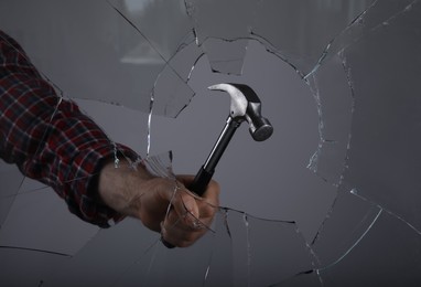 Photo of Man breaking window with hammer on grey background, closeup