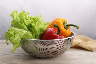 Photo of Colander with fresh lettuce and bell peppers on wooden table