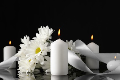 White chrysanthemum flowers and burning candles on black mirror surface in darkness. Funeral symbols