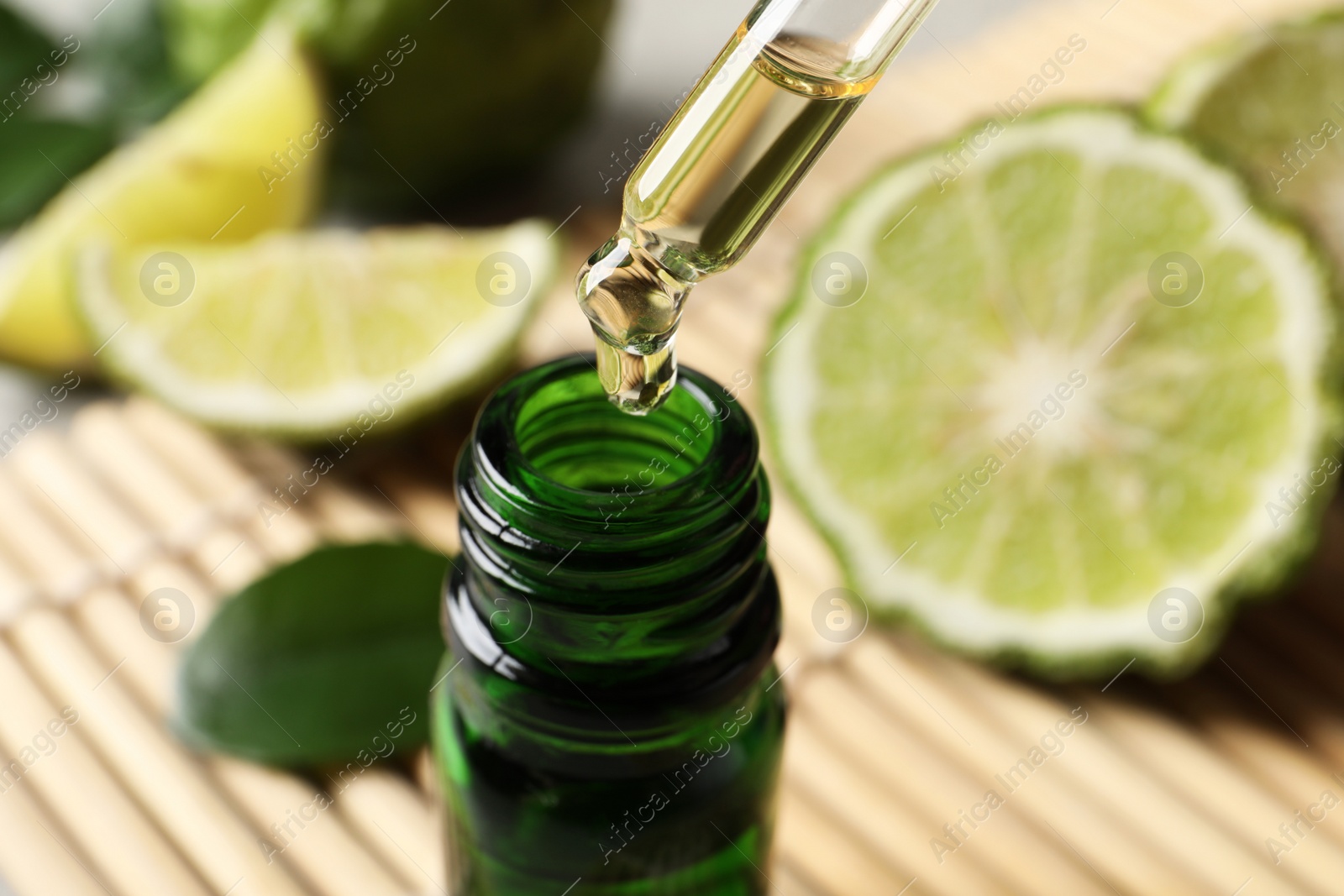 Photo of Dripping bergamot essential oil into glass bottle on table, closeup