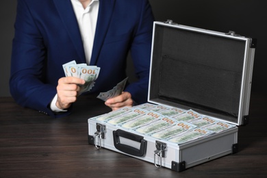 Businessman with case of dollar bills at wooden table, closeup