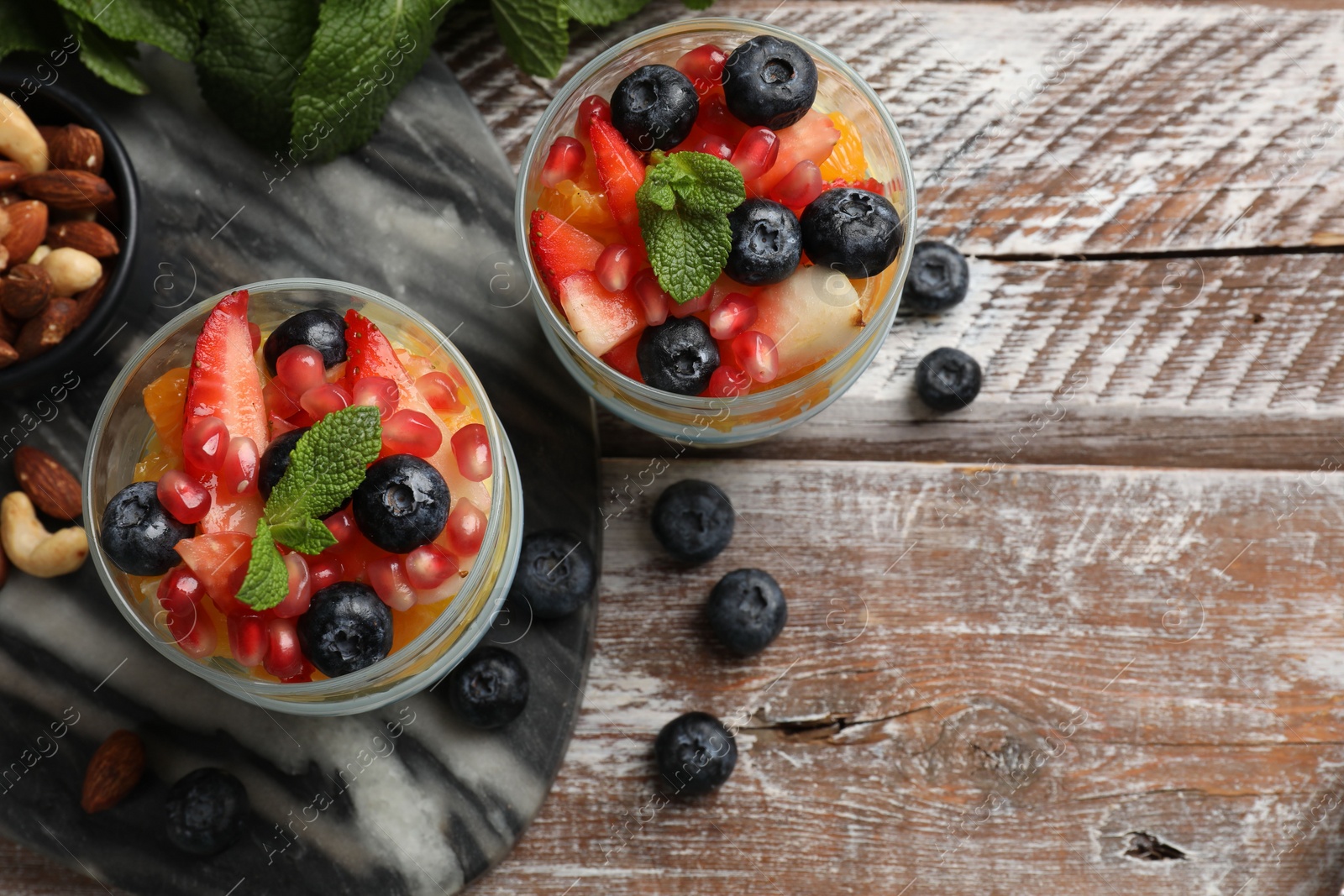 Photo of Delicious fruit salad, fresh berries, mint and nuts on wooden table, flat lay. Space for text