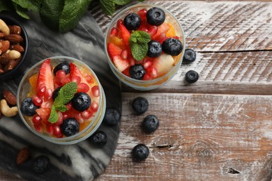 Delicious fruit salad, fresh berries, mint and nuts on wooden table, flat lay. Space for text