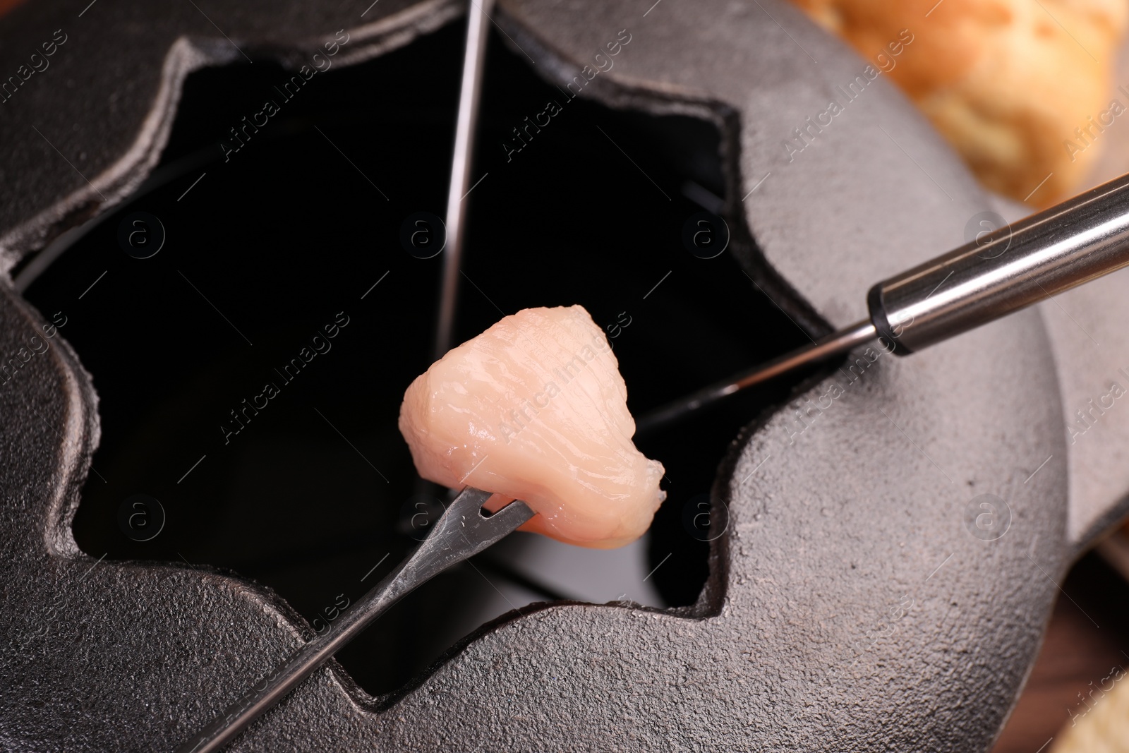 Photo of Fondue pot, forks and piece of raw meat on table, closeup