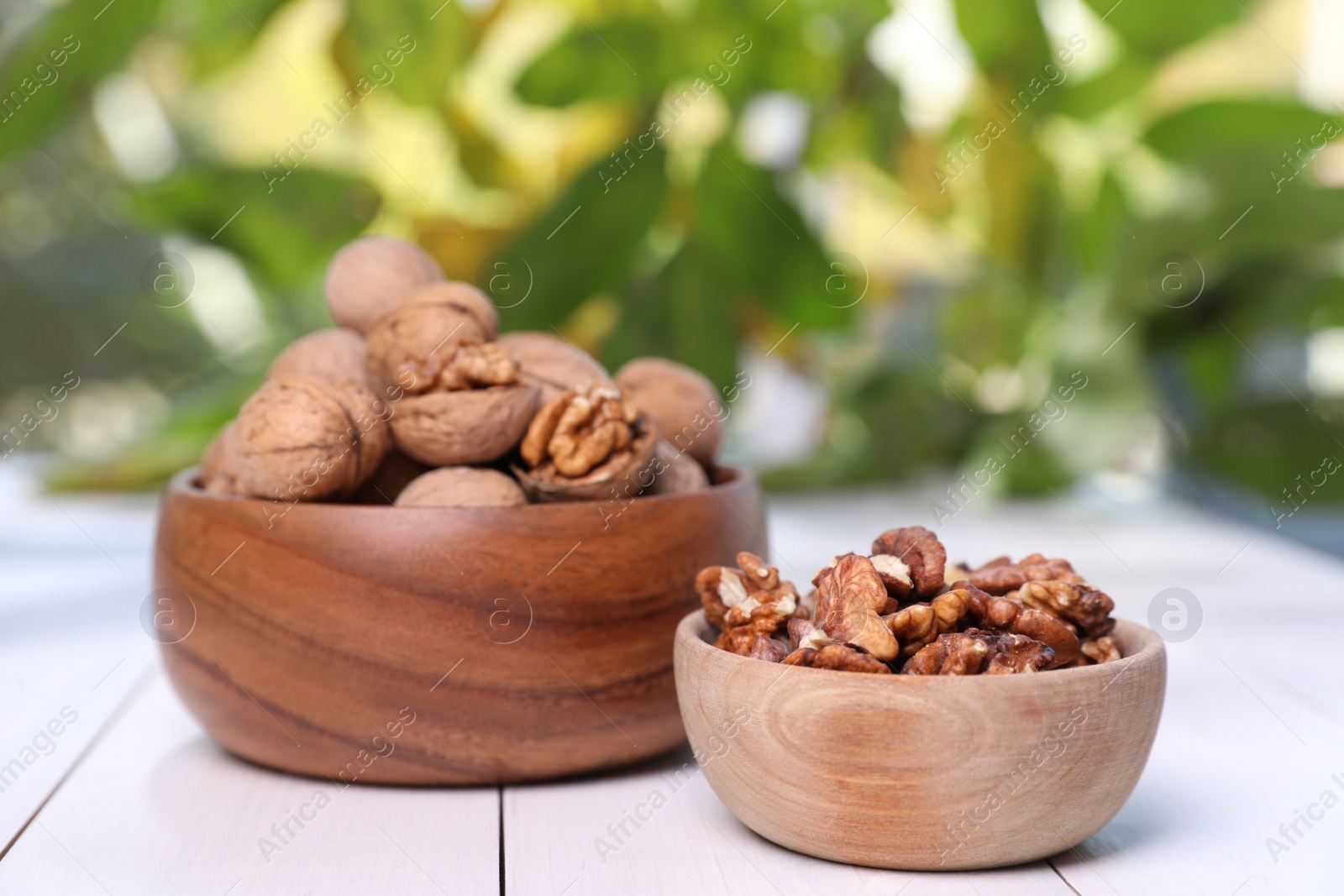 Photo of Bowls with walnuts on white wooden table outdoors