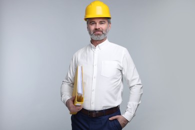 Architect in hard hat holding folder on grey background