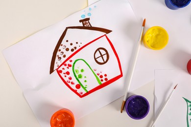 Cute children's drawing, brushes and set of paints on white table, flat lay