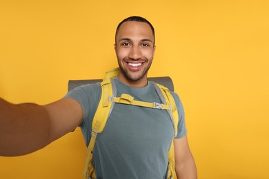Photo of Happy tourist with backpack taking selfie on yellow background