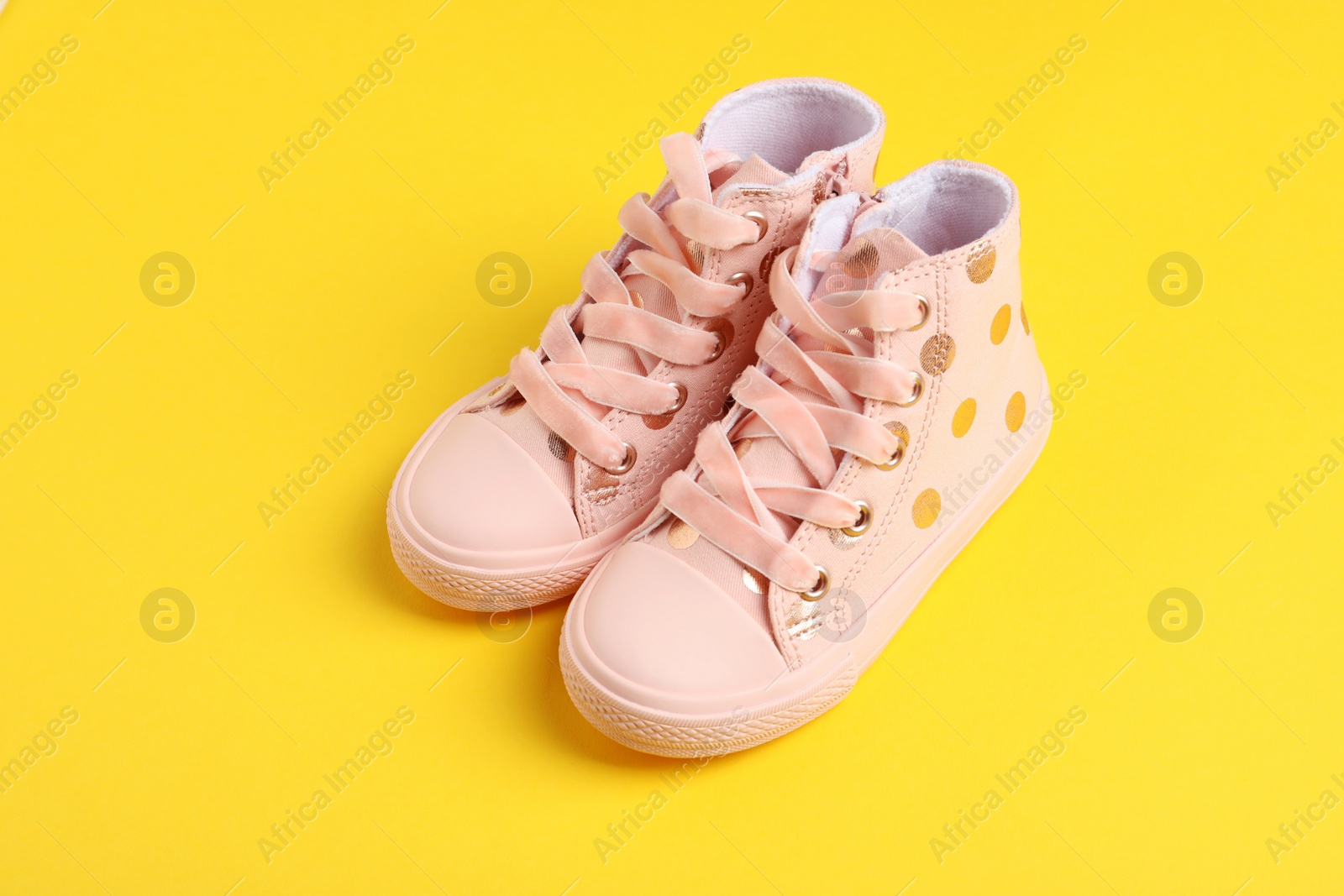 Photo of Pair of stylish child shoes on yellow background