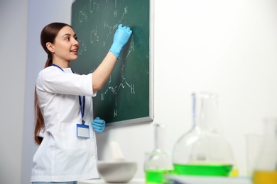 Female scientist writing chemical formula on chalkboard indoors, space for text