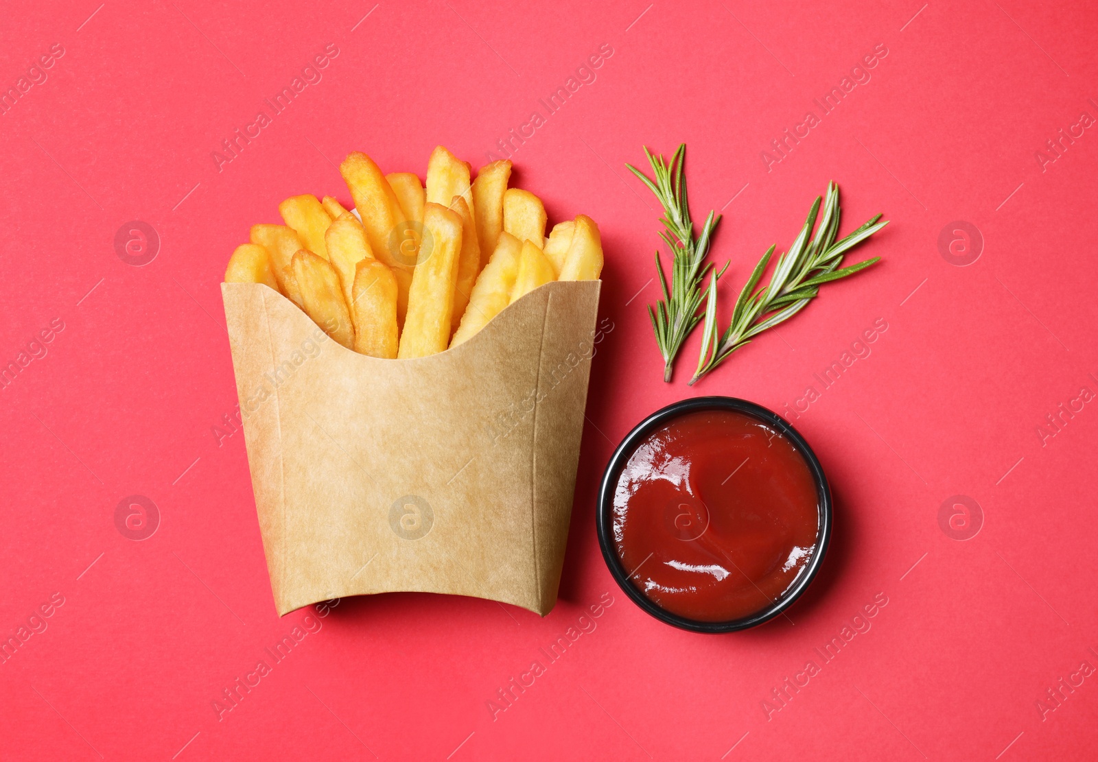 Photo of Paper cup with French fries, rosemary and ketchup on red table, flat lay
