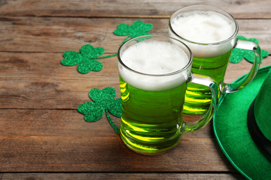 Photo of Green beer, hat and clover leaves on wooden table, space for text. St. Patrick's Day celebration