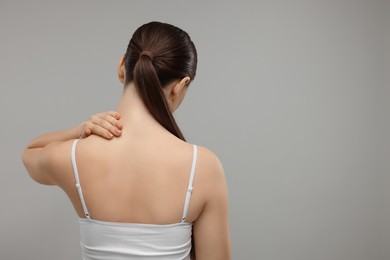 Woman touching her neck on grey background, back view. Space for text