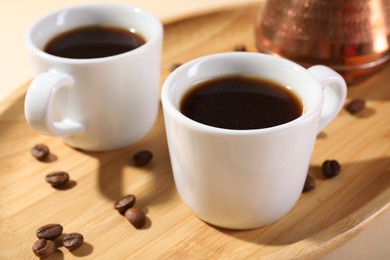 Photo of Delicious coffee in cups and beans on wooden board, closeup