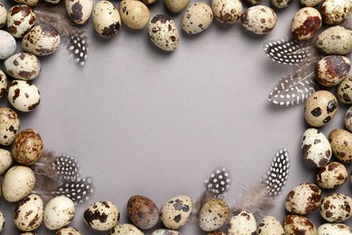 Photo of Frame made of speckled quail eggs and feathers on light grey background, flat lay. Space for text
