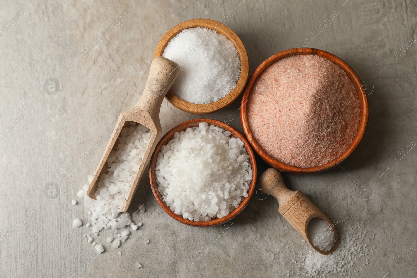 Photo of Different natural salt on grey textured table, flat lay