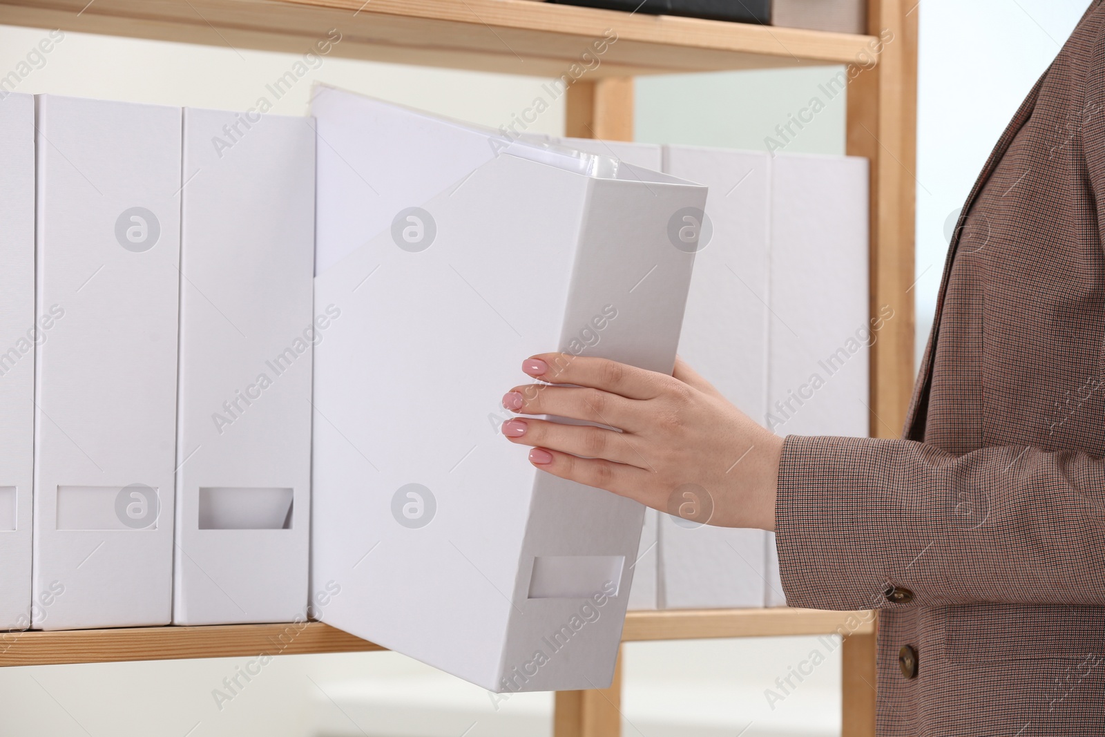 Photo of Woman taking folder with documents from shelf in office, closeup