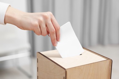 Photo of Woman putting her vote into ballot box on blurred background, closeup