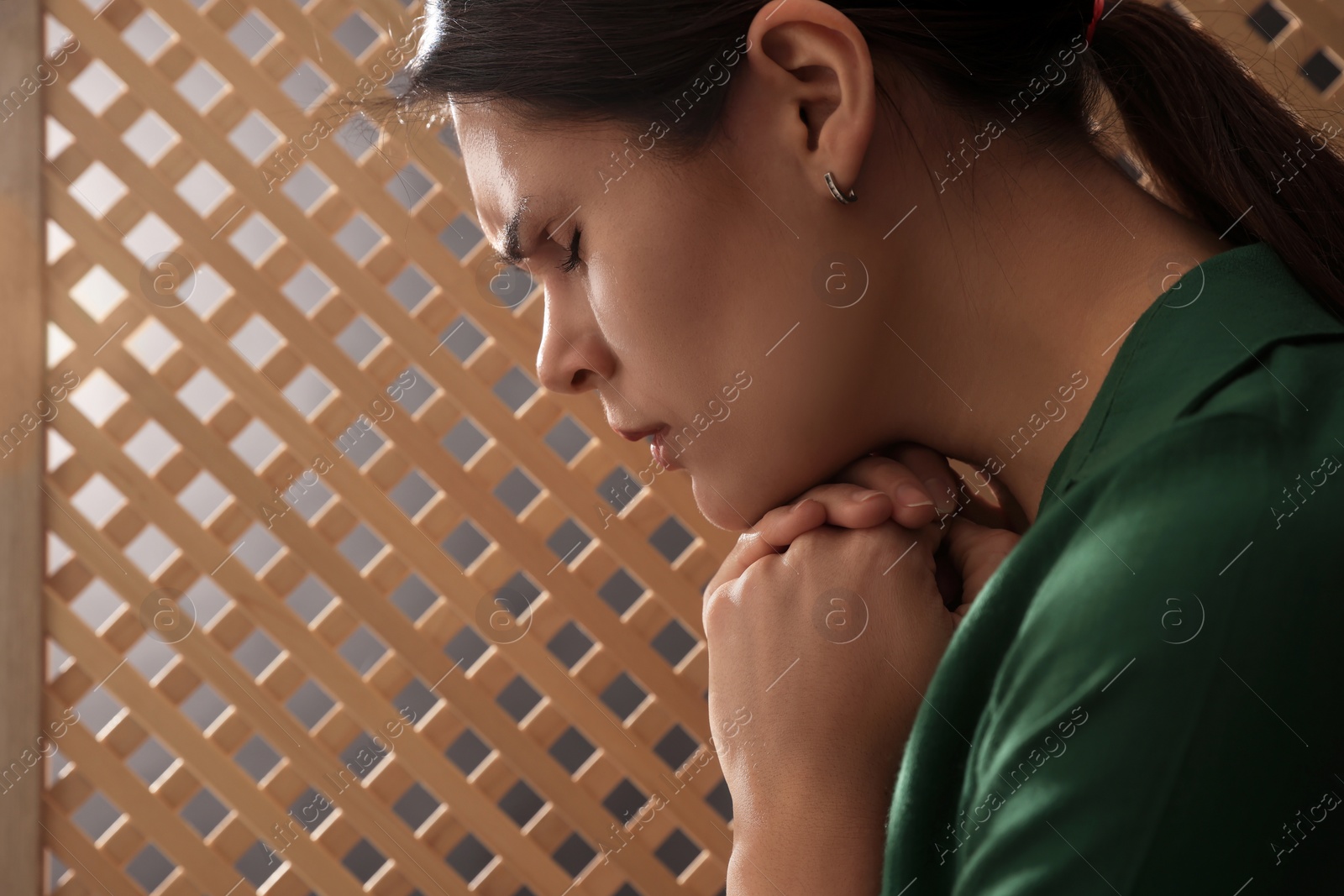 Photo of Upset woman listening to priest during confession in booth