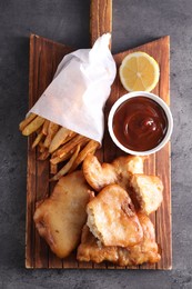 Photo of Tasty fish, chips and sauce on grey table, top view