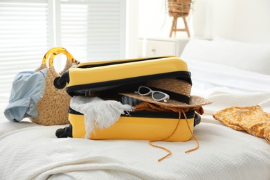 Photo of Open suitcase full of clothes and summer accessories on bed in room