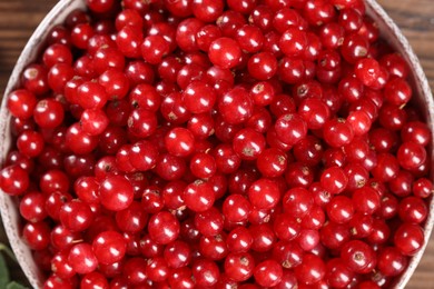 Photo of Ripe red currants and leaves in bowl on table, top view