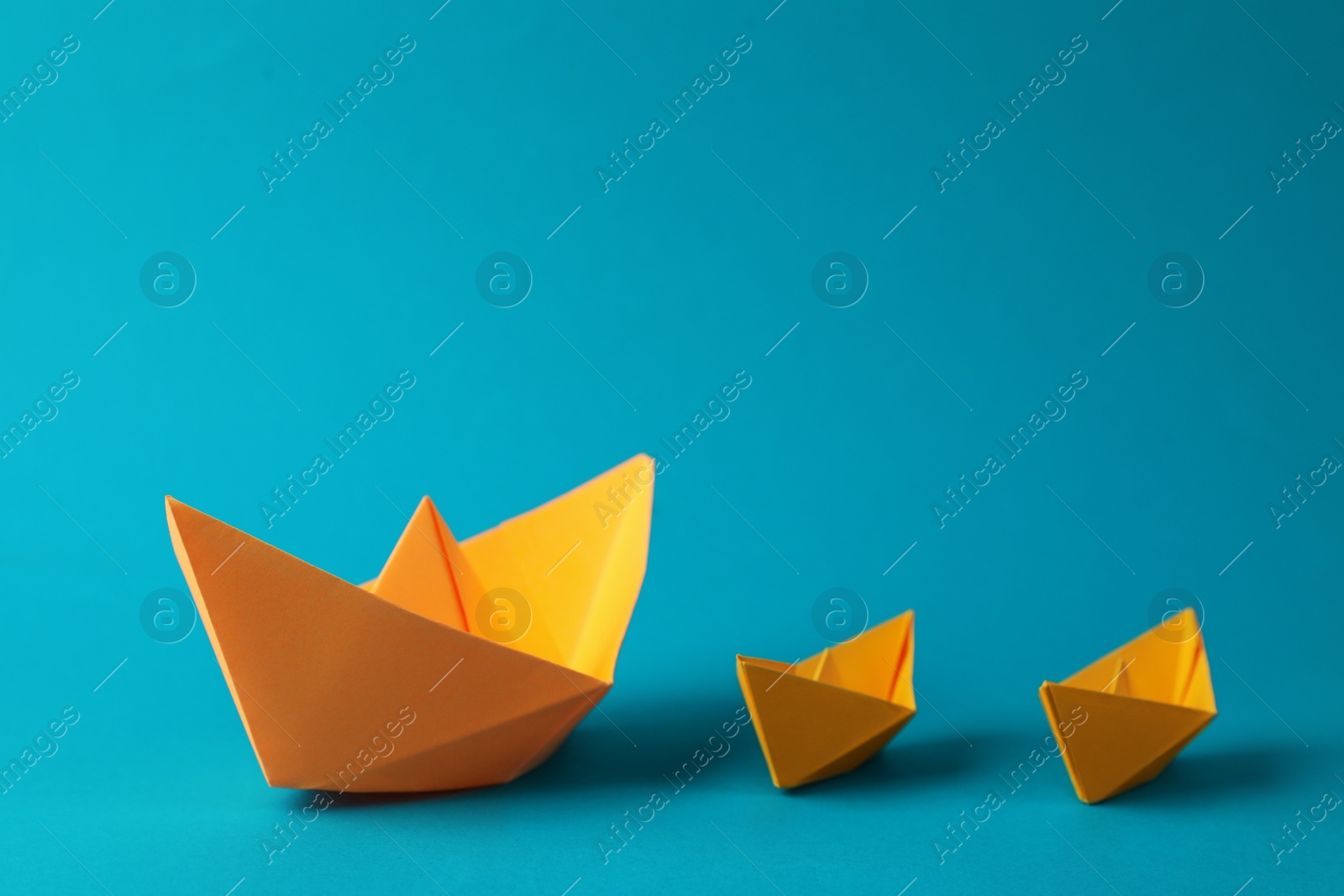 Photo of Many handmade orange paper boats on light blue background. Origami art