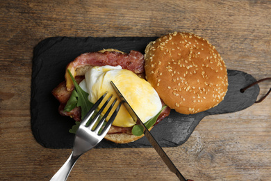 Photo of Cutting tasty egg Benedict on slate board, top view