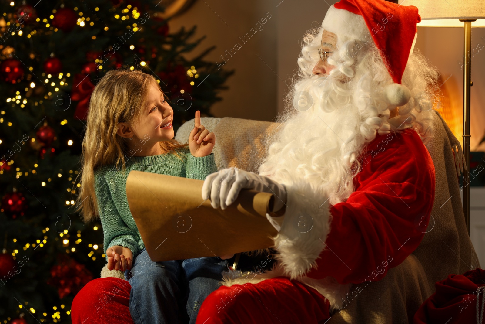Photo of Little girl with Santa Claus near Christmas tree in room