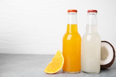 Delicious kombucha in glass bottles, coconut and orange on grey table against white background, space for text