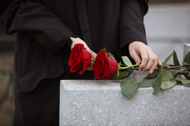 Woman with red roses near light grey tombstone outdoors, closeup. Funeral ceremony