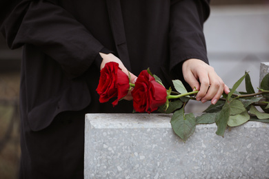 Photo of Woman with red roses near light grey tombstone outdoors, closeup. Funeral ceremony