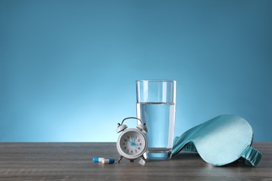 Photo of Alarm clock, soporific pills, sleeping mask and glass of water on wooden table, space for text. Insomnia treatment