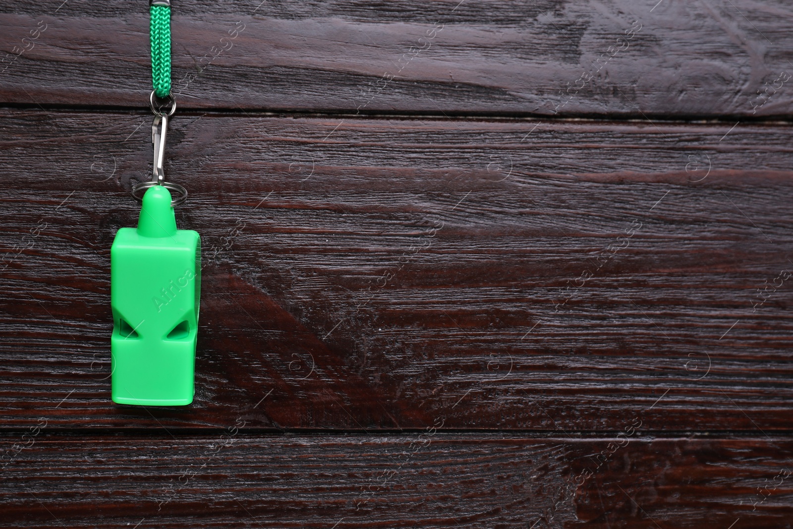 Photo of One green whistle with cord on wooden table, top view. Space for text