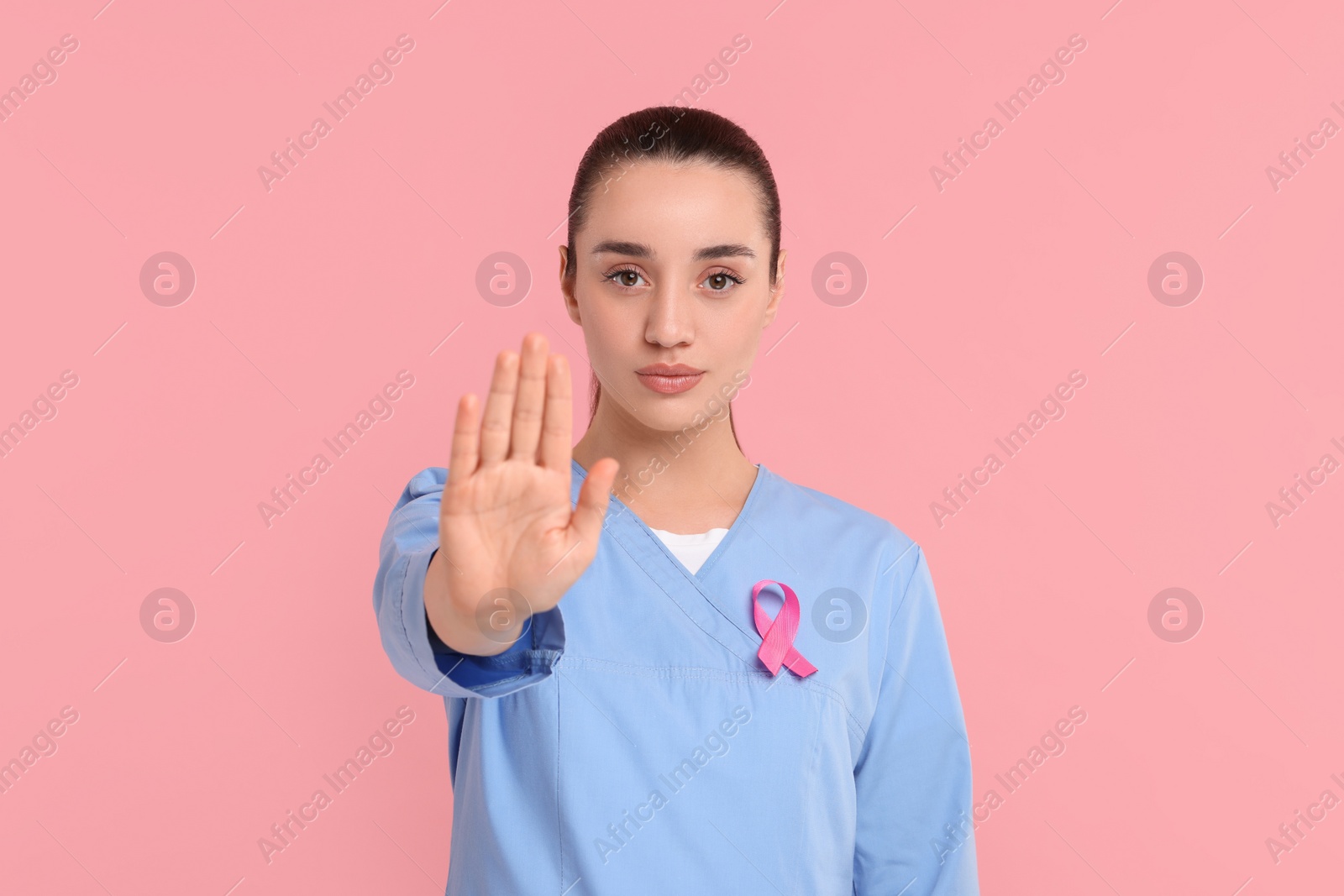 Photo of Mammologist with pink ribbon showing stop gesture on color background. Breast cancer awareness