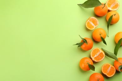 Photo of Fresh tangerines with green leaves on light green background, flat lay. Space for text