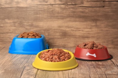 Dry and wet pet food in feeding bowls on wooden floor