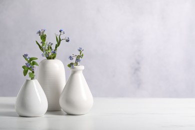 Photo of Beautiful forget-me-not flowers in vases on white marble table, closeup. Space for text