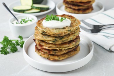 Photo of Delicious zucchini pancakes with sour cream served on light grey table