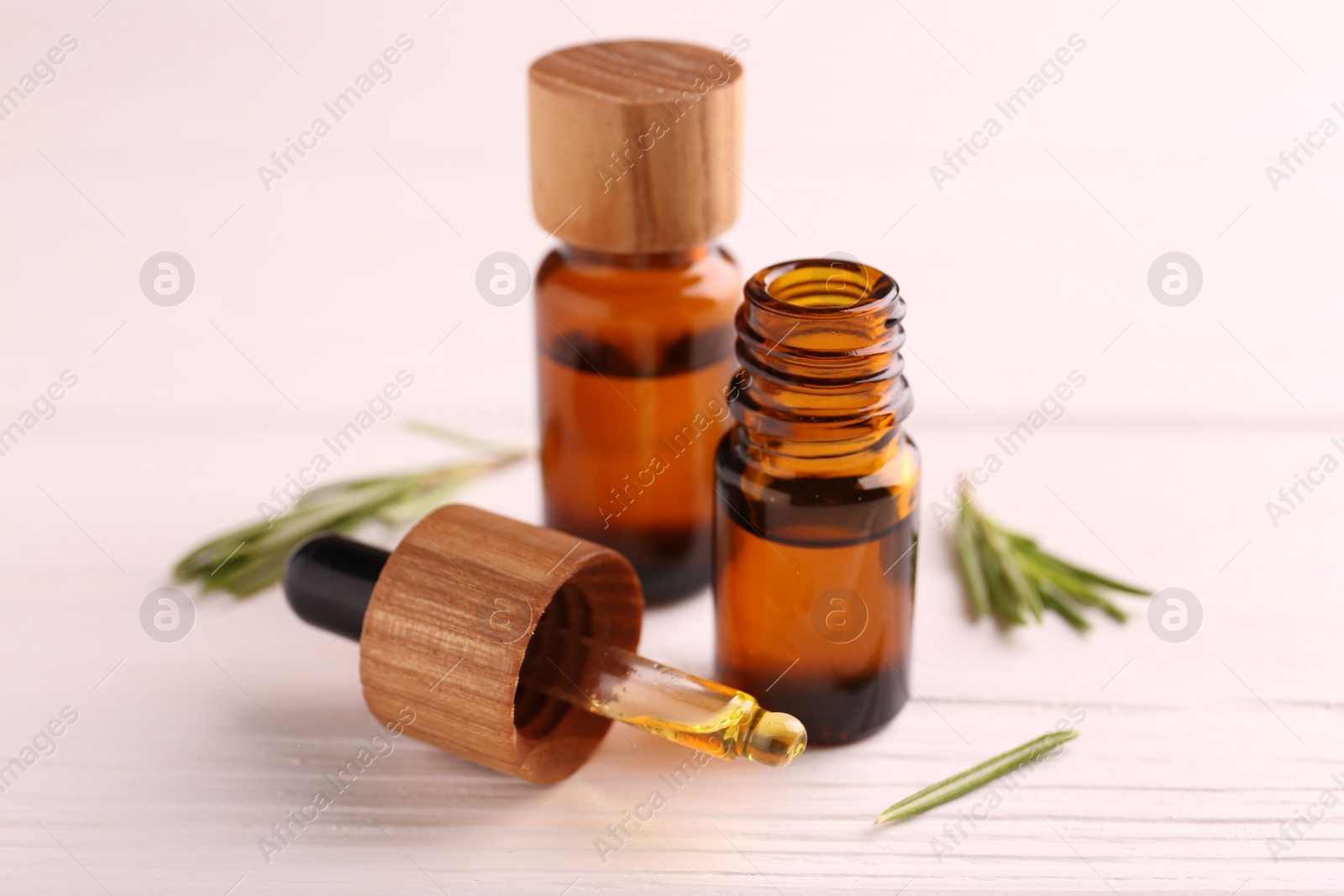 Photo of Essential oil in bottles, dropper and rosemary on white wooden table, closeup