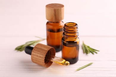 Photo of Essential oil in bottles, dropper and rosemary on white wooden table, closeup