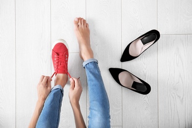 Young woman changing shoes on wooden background, top view