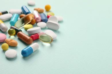 Pile of different pills on mint background, selective focus. Space for text