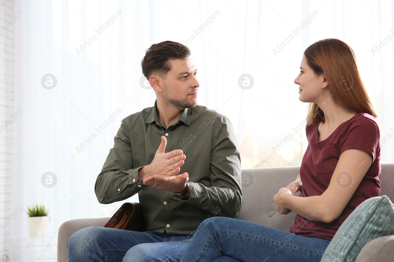 Photo of Hearing impaired friends using sign language for communication on sofa in living room