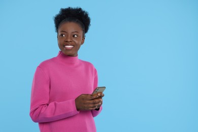 Photo of Happy young woman with smartphone on light blue background. Space for text