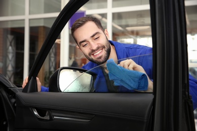 Worker cleaning automobile window glass with rag at car wash