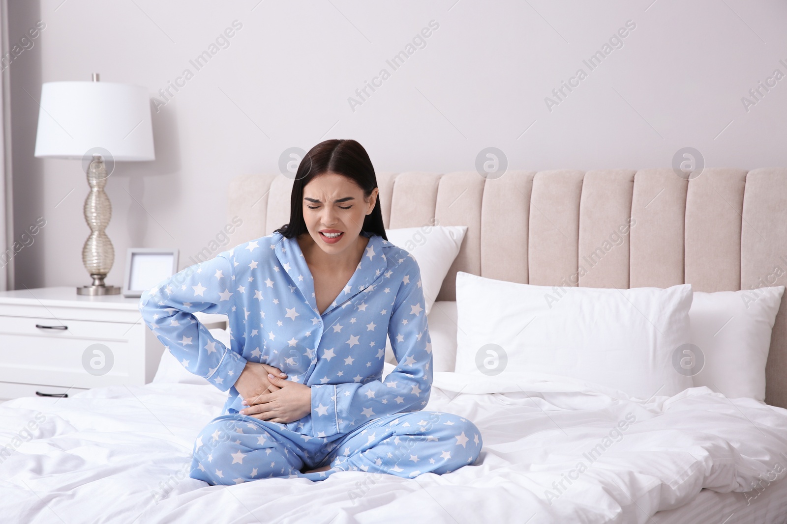 Photo of Young woman suffering from stomach ache in bedroom