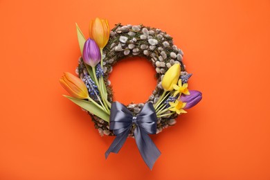 Willow wreath with different beautiful flowers and grey bow on orange background, top view