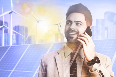 Multiple exposure of businessman with smartphone, wind turbines and solar panels installed outdoors. Alternative energy source