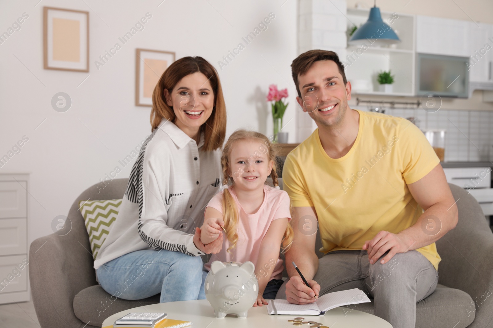 Photo of Happy family putting coin into piggy bank at table indoors. Saving money